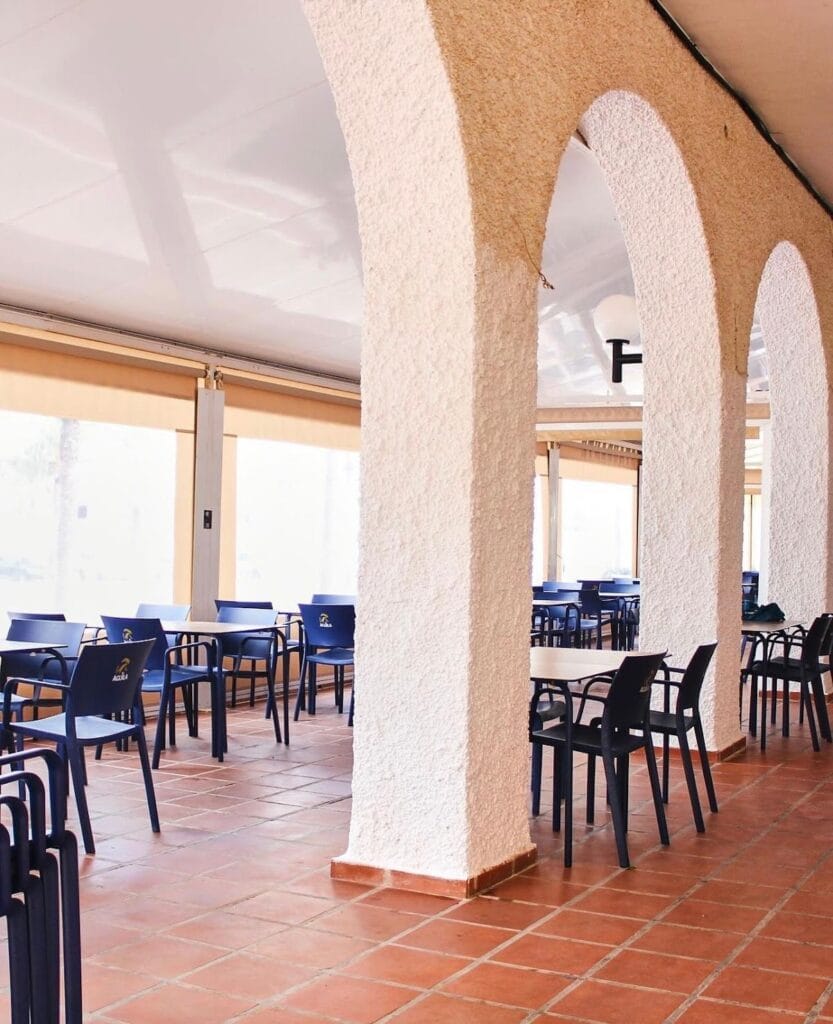 Comedor porticado del Restaurante El Murciano con arcos blancos de yeso, suelo de barro cocido y sillas azules, luz natural tamizada
