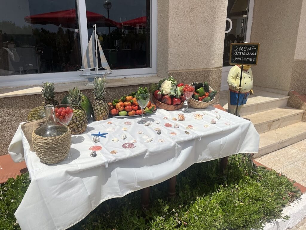 Mesa decorativa de bienvenida en Restaurante La Balandra con frutas frescas, verduras y conchas marinas al aire libre