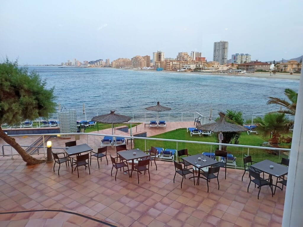 Terraza del Restaurante Hotel Galúa con mesas frente al Mar Menor y vistas al skyline de La Manga del Mar Menor al atardecer