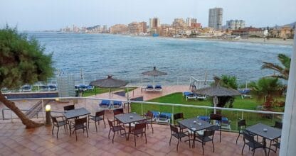 Terraza del Restaurante Hotel Galúa con mesas frente al Mar Menor y vistas al skyline de La Manga del Mar Menor al atardecer
