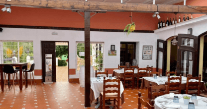 Amplio comedor del Restaurante La Rusticana con suelo de barro rojo, mesas con mantel blanco y luz natural entrando por ventanales