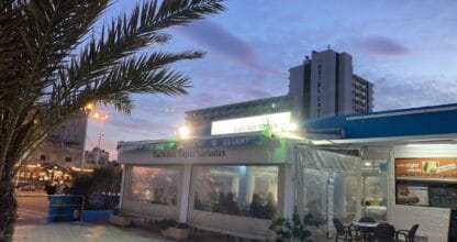 Exterior nocturno del Café Bar Nino's en La Manga del Mar Menor, con terraza acristalada y letrero de raciones y tapas variadas