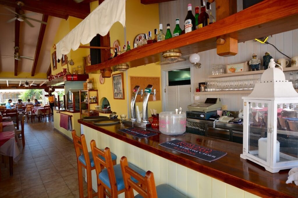 Barra interior del Restaurante Pizzería Amsterdam con grifos de cerveza, estantería de licores y decoración amarilla