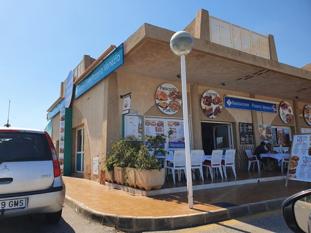 Fachada exterior de Restaurante Pizzería Venezia con rótulos de pescado, paella y carnes en La Manga