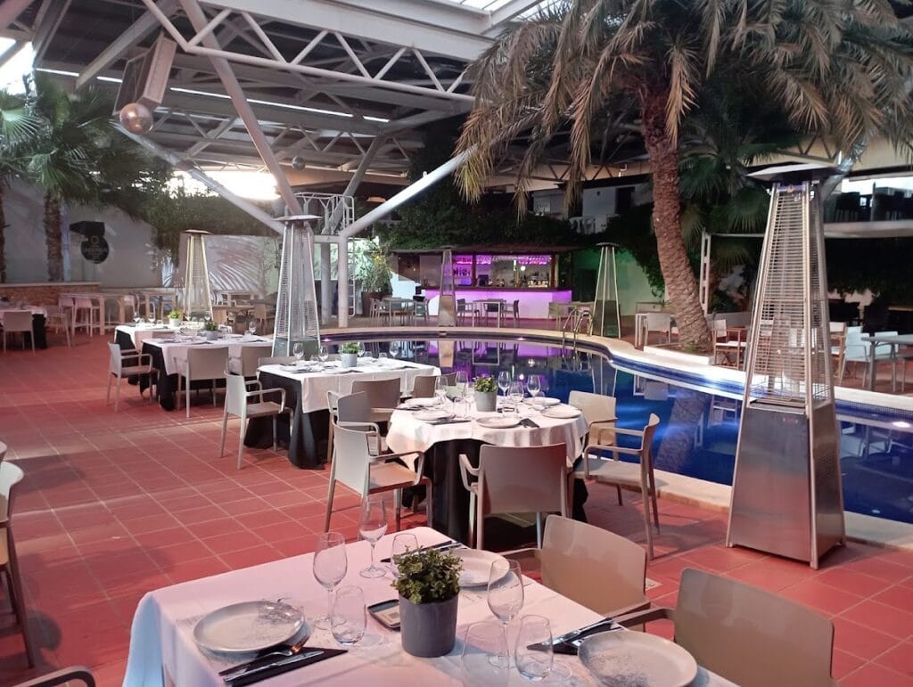 Terraza cubierta con mesas vestidas de blanco, calefactores y piscina iluminada en Ristorante Birbantello, La Manga del Mar Menor
