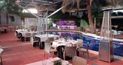 Terraza cubierta con mesas vestidas de blanco, calefactores y piscina iluminada en Ristorante Birbantello, La Manga del Mar Menor