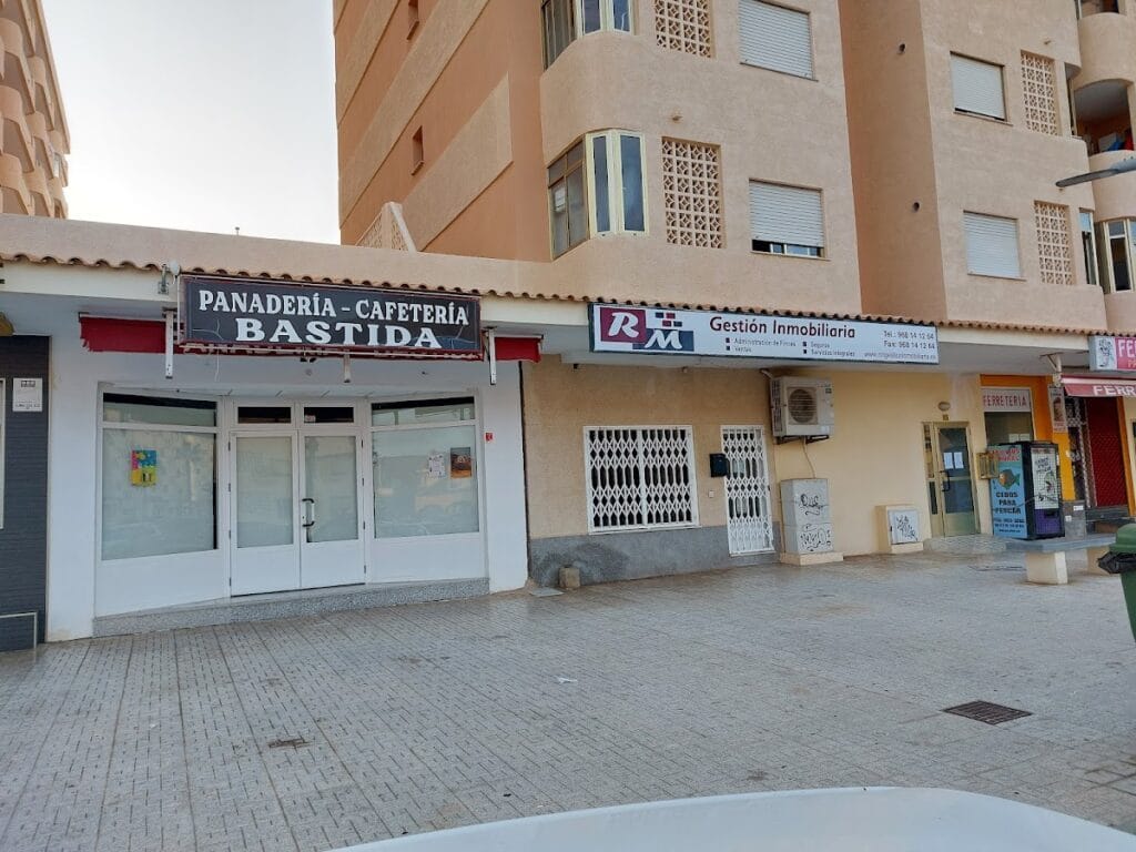 Fachada de RM Gestión Inmobiliaria junto a panadería Bastida en bloque residencial de La Manga del Mar Menor