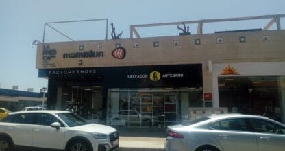 Fachada exterior de la zapatería Salvador Artesano en zona comercial con Factory Shoes, coches aparcados y estructura de madera en la cubierta