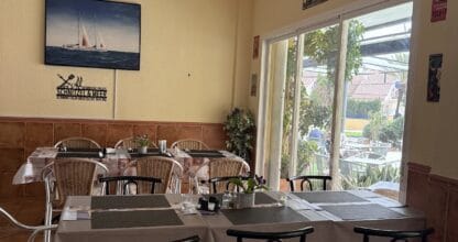 Sala interior del restaurante Schnitzel und Meer Bistro con mesas dispuestas, cuadro marinero y vistas al jardín exterior