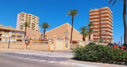 Edificio de estilo mediterráneo con palmeras y torres residenciales junto a la avenida principal de La Manga del Mar Menor