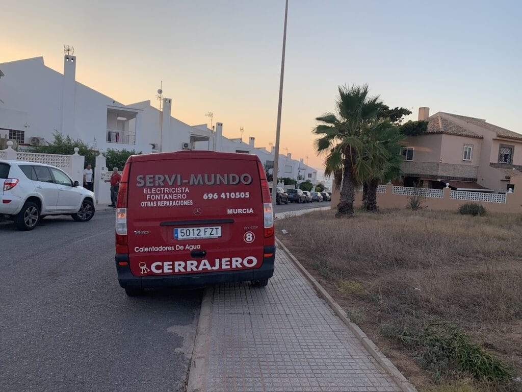 Furgoneta roja de SERVI-MUNDO Cerrajero con rótulos de electricista y fontanero en zona residencial de La Manga