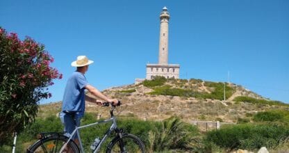 Ciclista con bicicleta y sombrero de paja frente al faro de Cabo de Palos, alquiler de bicicletas SOBIKES