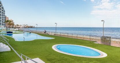 Zonas comunes con piscinas y césped verde frente al Mar Menor en urbanización gestionada por SoleaHost