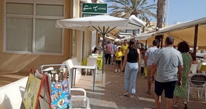 Calle peatonal animada de La Manga del Mar Menor con terrazas de bares, palmeras y turistas paseando junto a Spar Express