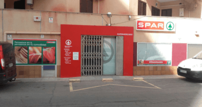 Fachada roja del supermercado Spar con rótulo de alimentación y puerta metálica enrollable en La Manga del Mar Menor