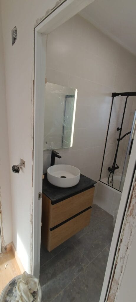 Baño reformado con lavabo redondo, mueble de madera y mampara negra por Summer Solution Cartagena
