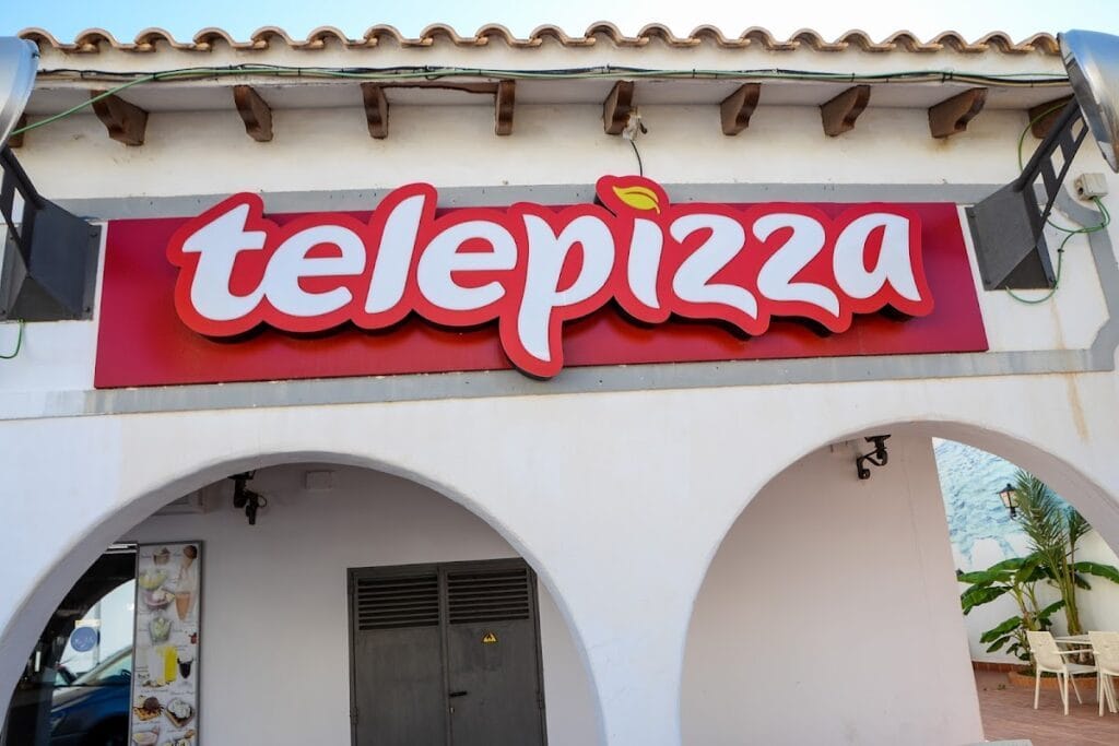 Rótulo luminoso rojo de Telepizza en La Manga del Mar Menor sobre fachada blanca con arcos de estilo mediterráneo