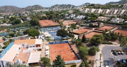 Vista aérea del Racquets Club de La Manga Club con pistas de tenis de tierra batida y pistas de pádel rodeadas de vegetación y urbanizaciones