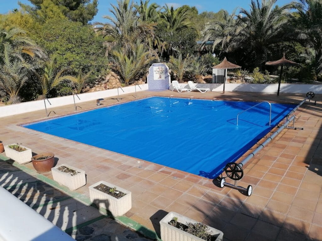 Piscina cubierta con lona isotérmica azul y palmeras en jardín, instalada por TOLDHOGAR en La Manga del Mar Menor