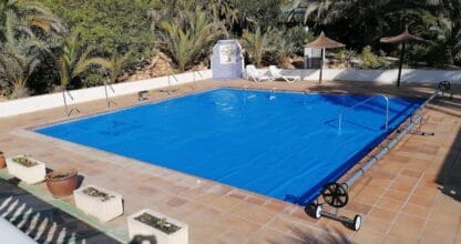 Piscina cubierta con lona isotérmica azul y palmeras en jardín, instalada por TOLDHOGAR en La Manga del Mar Menor