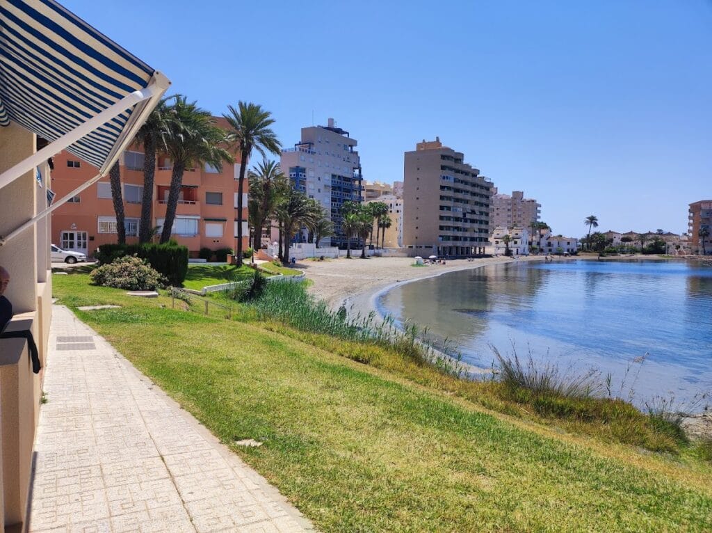 Paseo junto a la playa de Urbanización Bahía Cálida en La Manga del Mar Menor con edificios de apartamentos y palmeras