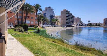 Paseo junto a la playa de Urbanización Bahía Cálida en La Manga del Mar Menor con edificios de apartamentos y palmeras
