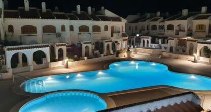 Urbanización Villas Mediterráneo en La Manga del Mar Menor con piscina comunitaria iluminada de noche y bungalows de estilo andaluz