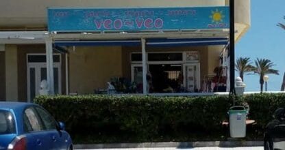 Fachada de Veo-Veo prensa y revistas en La Manga del Mar Menor con toldo azul y palmeras al fondo