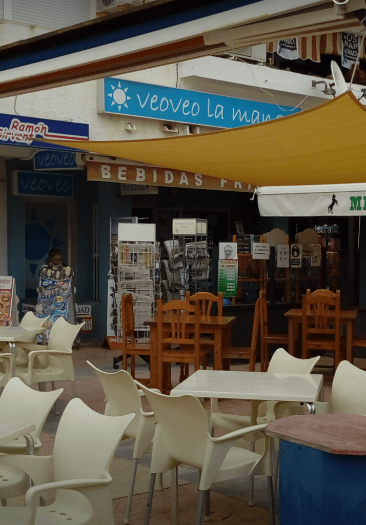Terraza exterior de Veo~Veo Bohemia con mesas y sillas blancas bajo toldo amarillo en La Manga del Mar Menor