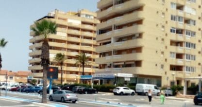 Avenida principal de La Manga del Mar Menor con edificios de apartamentos altos, palmeras y tráfico rodado