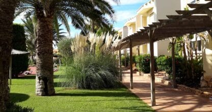 Jardines de Villas La Manga con palmeras, césped verde, plantas ornamentales y pérgola de madera en zona residencial
