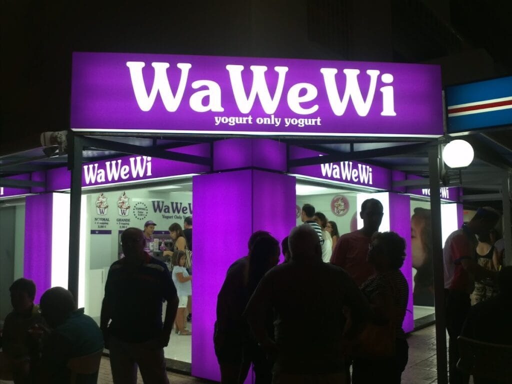 Puesto WaWeWi de yogurt iluminado en morado con clientes haciendo cola por la noche en La Manga del Mar Menor