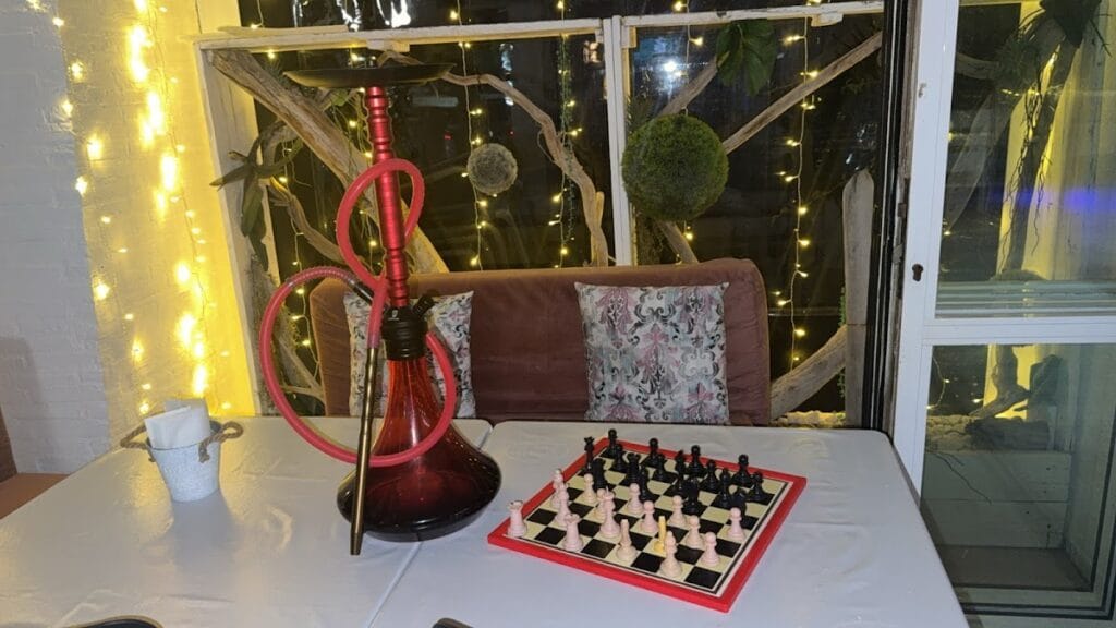 Interior íntimo del White Diamond con cachimba roja, tablero de ajedrez sobre mesa y decoración de luces LED y madera envejecida
