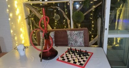 Interior íntimo del White Diamond con cachimba roja, tablero de ajedrez sobre mesa y decoración de luces LED y madera envejecida