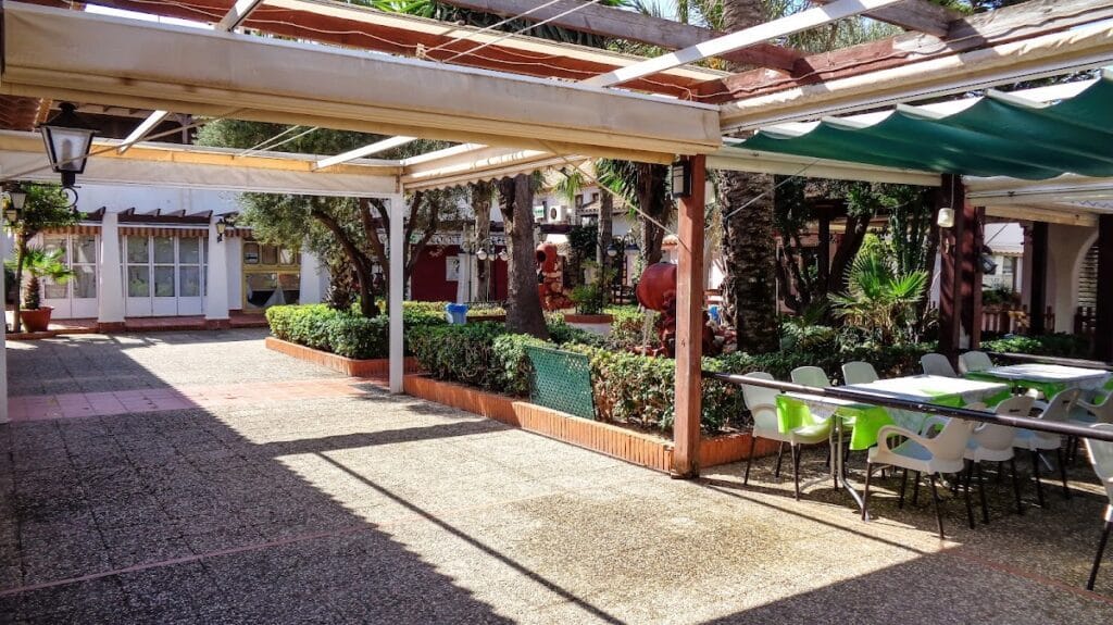 Terraza sombreada con mesas y sillas del Zoco La Manga con zona ajardinada y ambiente de centro comercial al aire libre