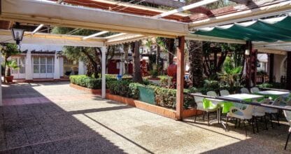 Terraza sombreada con mesas y sillas del Zoco La Manga con zona ajardinada y ambiente de centro comercial al aire libre
